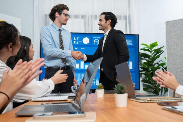Two businessman shake hand in meeting room with coworker give cheerful applause. Team of analyst celebrate after successful significant progress on business strategic performance. Habiliment